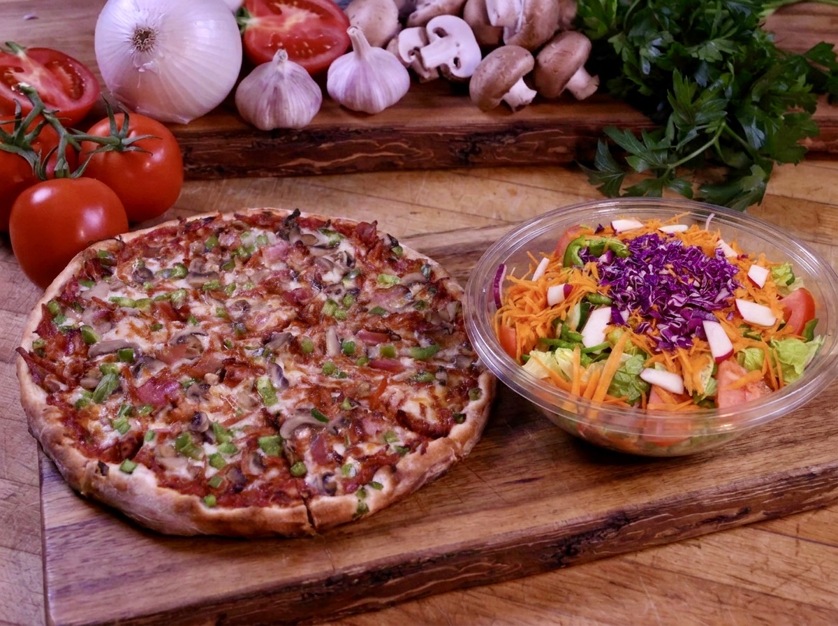 Capri pizza topped with bacon, mushrooms and green peppers beside a bowl of fresh garden salad.